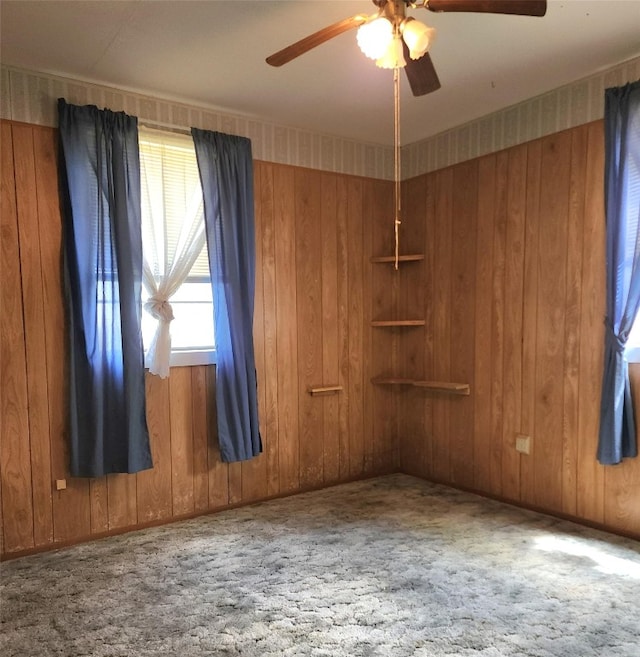 carpeted spare room featuring wooden walls, ceiling fan, and a healthy amount of sunlight