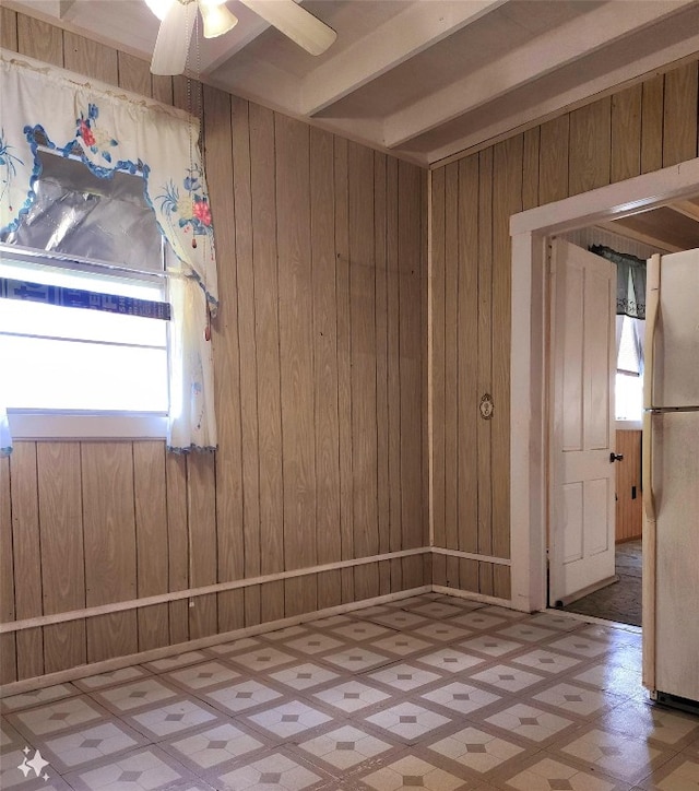 spare room with ceiling fan, beam ceiling, and wooden walls