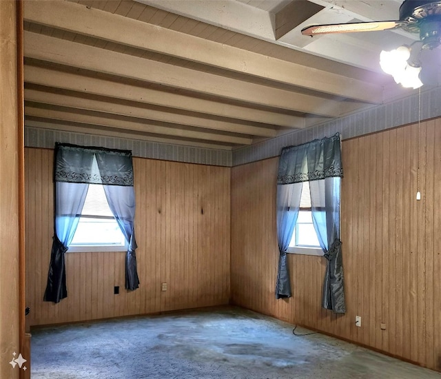 empty room featuring wood walls, ceiling fan, concrete floors, and beamed ceiling