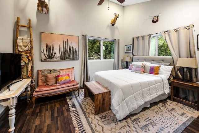 bedroom featuring wood finished floors, ceiling fan, multiple windows, and a towering ceiling
