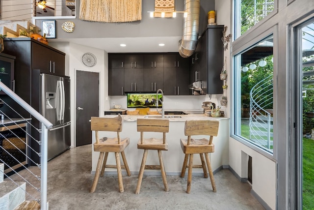 kitchen with stainless steel refrigerator with ice dispenser, a peninsula, concrete floors, and a sink