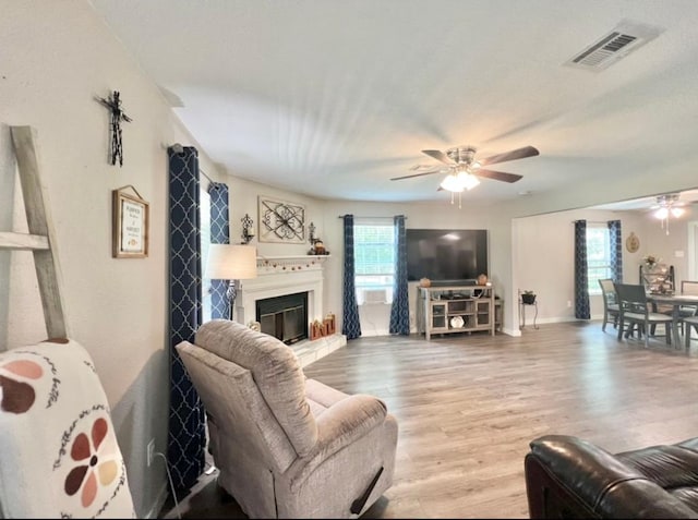 living area with a glass covered fireplace, wood finished floors, visible vents, and a ceiling fan