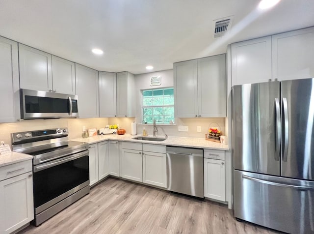 kitchen with light wood-type flooring, stainless steel appliances, light stone counters, and sink