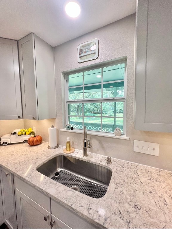 interior details with gray cabinetry, light stone counters, and sink