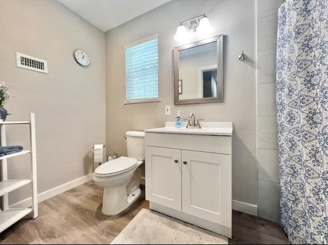 bathroom featuring visible vents, toilet, vanity, wood finished floors, and baseboards