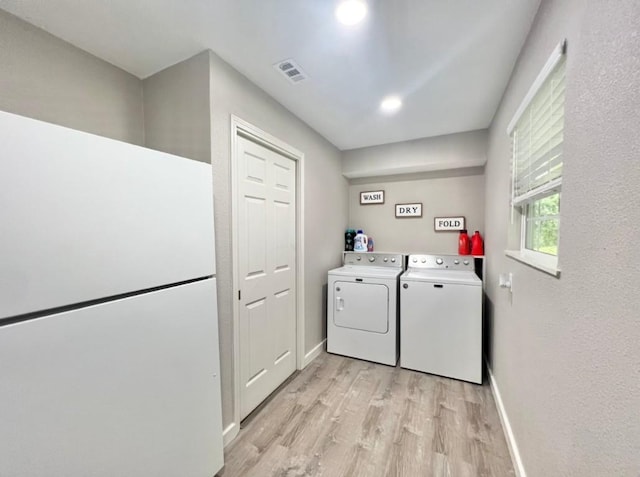 laundry room featuring washing machine and clothes dryer, visible vents, light wood-style flooring, laundry area, and baseboards