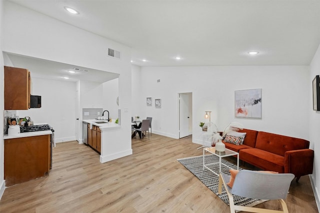 living room featuring sink, light hardwood / wood-style flooring, and high vaulted ceiling