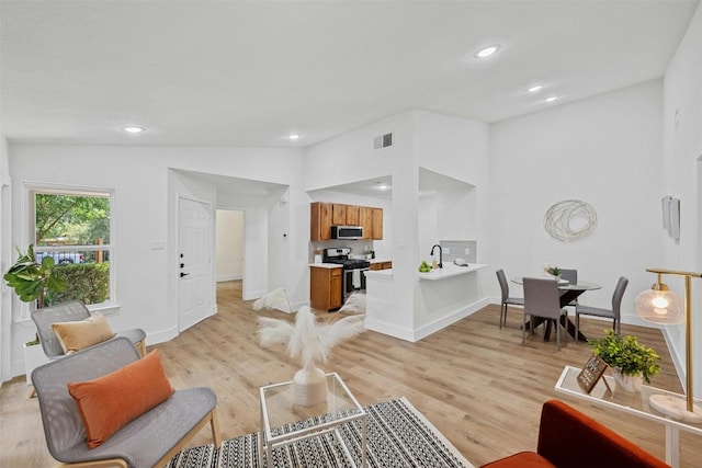 living room with light wood-type flooring, lofted ceiling, and sink