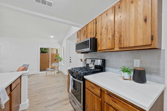 kitchen with light wood-type flooring, appliances with stainless steel finishes, tasteful backsplash, and vaulted ceiling