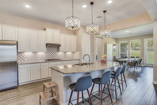 kitchen featuring tasteful backsplash, light hardwood / wood-style floors, sink, a center island with sink, and stainless steel appliances