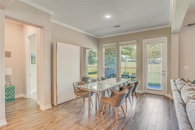 dining space with light hardwood / wood-style floors, a wealth of natural light, crown molding, and a textured ceiling