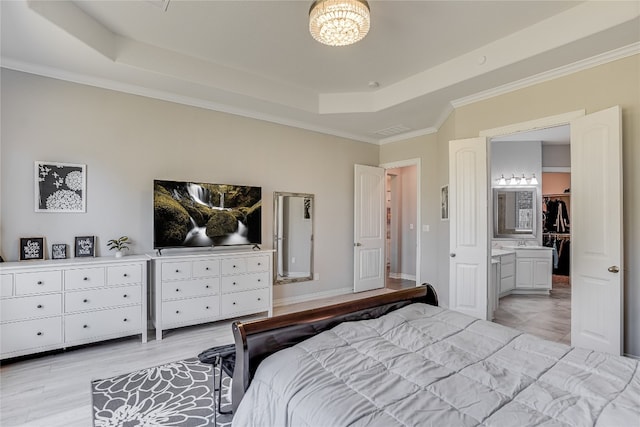 bedroom featuring light hardwood / wood-style floors, connected bathroom, ornamental molding, and a tray ceiling