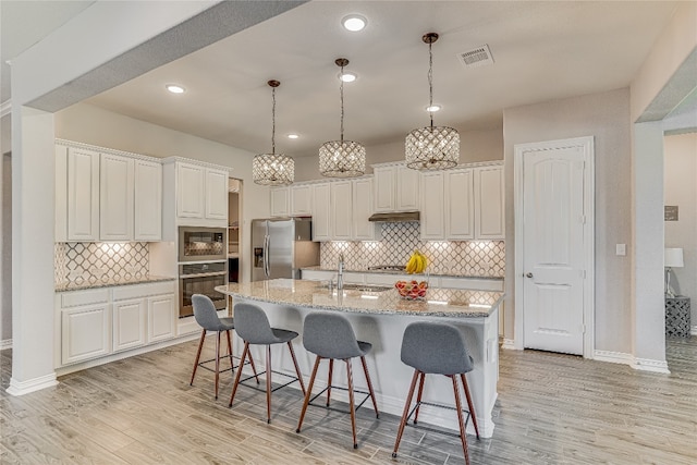 kitchen with stainless steel appliances, tasteful backsplash, sink, light wood-type flooring, and light stone countertops