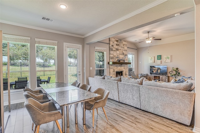 dining room featuring ceiling fan, light hardwood / wood-style flooring, ornamental molding, a fireplace, and a textured ceiling