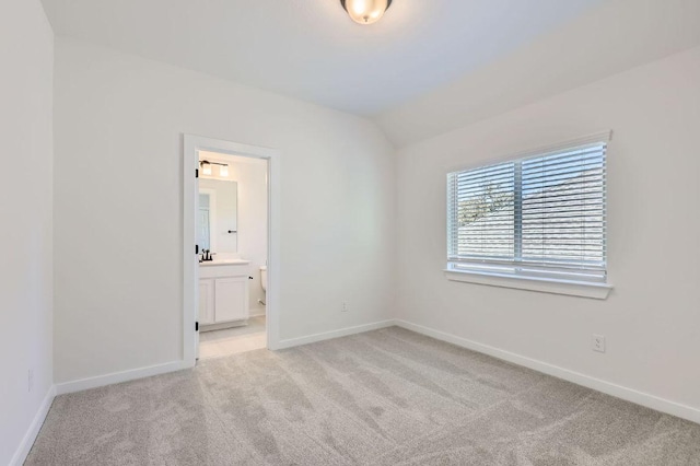 unfurnished bedroom with baseboards, light carpet, lofted ceiling, and ensuite bath