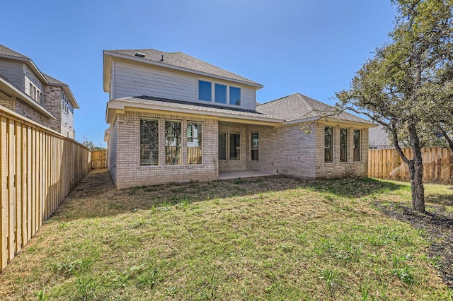 back of property with a fenced backyard, a patio, brick siding, and a yard