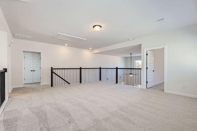 empty room with visible vents, light colored carpet, attic access, and baseboards