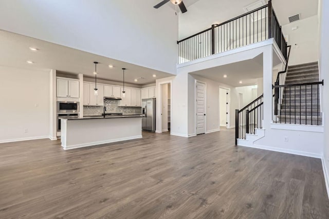 unfurnished living room featuring stairs, a sink, dark wood-style flooring, and ceiling fan