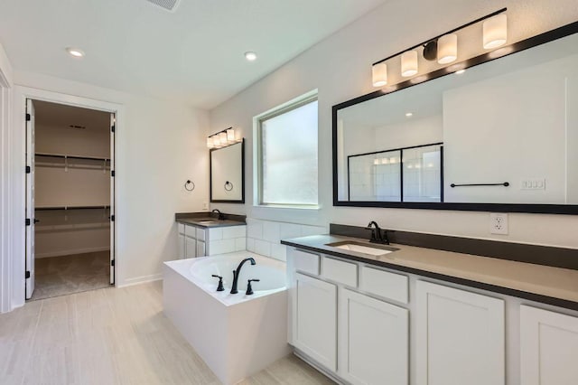 full bath featuring a sink, a garden tub, two vanities, and a shower stall