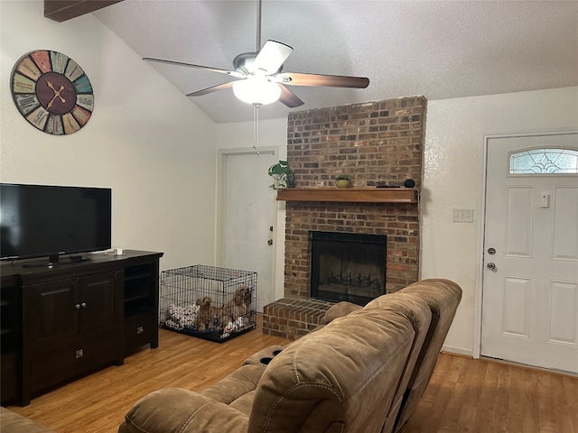 living room with ceiling fan, light wood-type flooring, vaulted ceiling, and a brick fireplace