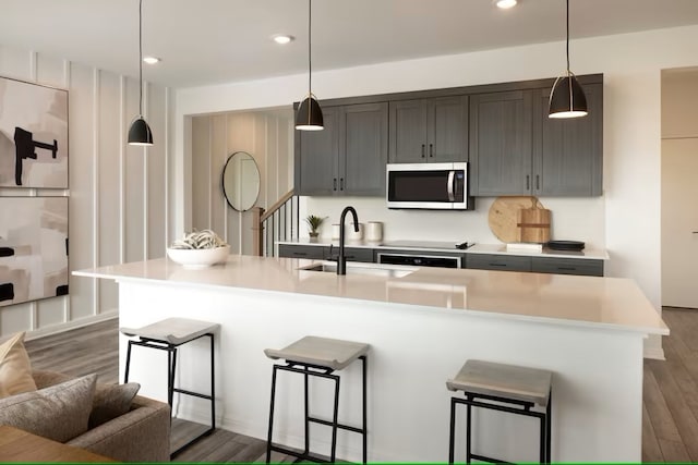 kitchen featuring a center island with sink, decorative light fixtures, dark wood-type flooring, and a breakfast bar area