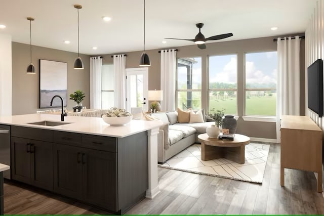 kitchen featuring ceiling fan, sink, decorative light fixtures, a center island with sink, and light hardwood / wood-style floors