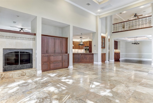 unfurnished living room featuring a tiled fireplace, ceiling fan with notable chandelier, light tile patterned floors, and crown molding