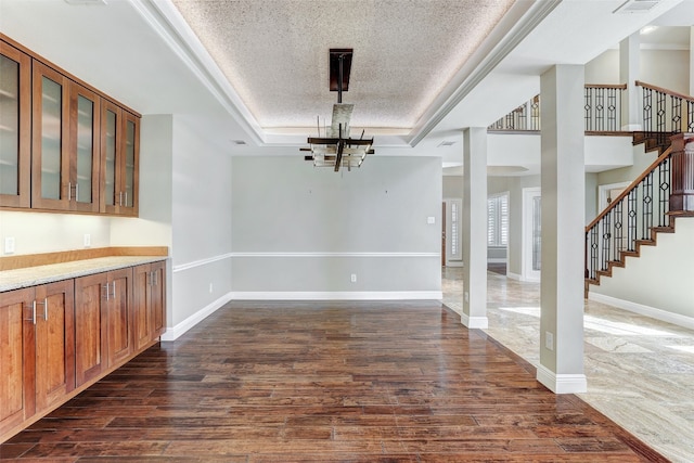 unfurnished dining area with an inviting chandelier, a textured ceiling, dark hardwood / wood-style flooring, and a tray ceiling