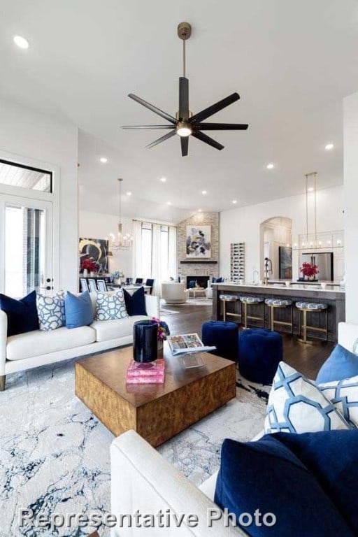 living room featuring light wood-type flooring, ceiling fan with notable chandelier, and a large fireplace