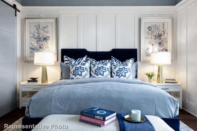 bedroom with a barn door and dark hardwood / wood-style floors