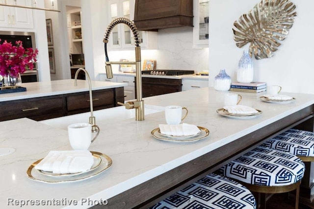 kitchen featuring light stone countertops, white cabinetry, dark brown cabinets, and tasteful backsplash