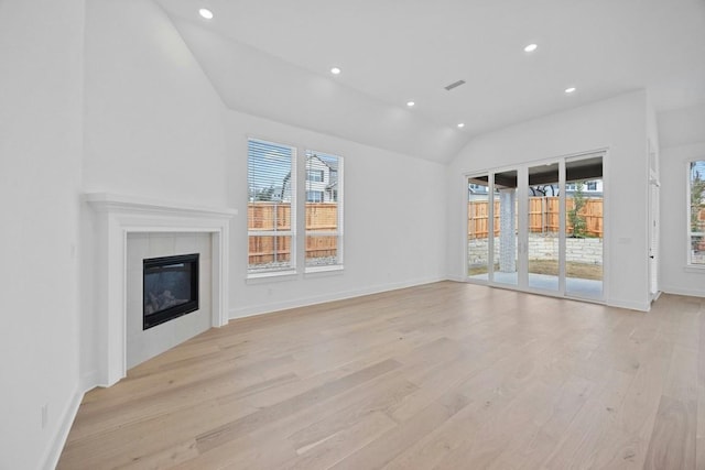 unfurnished living room with vaulted ceiling, a tile fireplace, and light hardwood / wood-style flooring