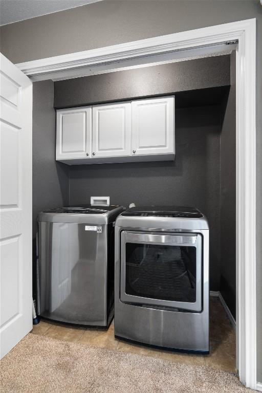 clothes washing area featuring washing machine and dryer, cabinets, and light tile patterned flooring