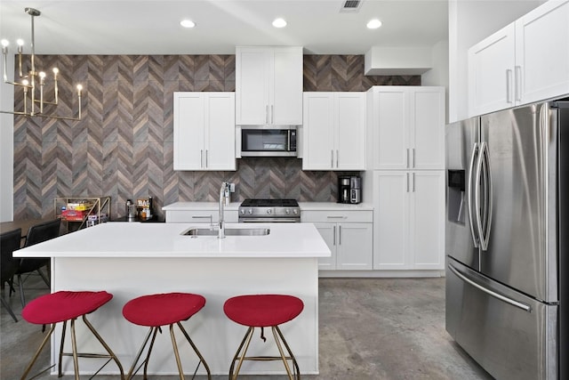 kitchen featuring appliances with stainless steel finishes, decorative light fixtures, sink, a kitchen island with sink, and white cabinets