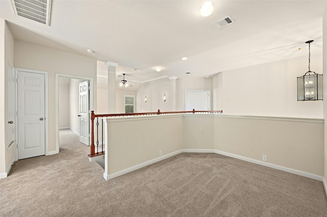 carpeted spare room with ceiling fan with notable chandelier and ornate columns