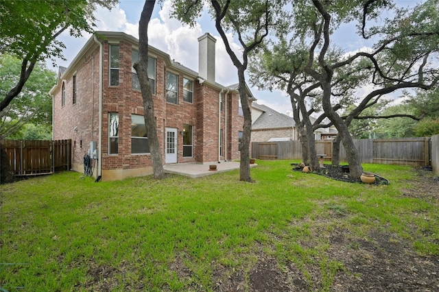 back of house with a yard, a fenced backyard, brick siding, and a chimney