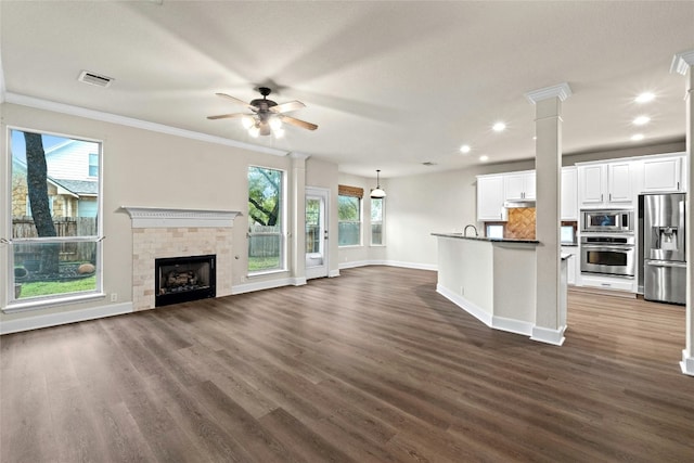 unfurnished living room with dark wood finished floors, visible vents, a tiled fireplace, and ornate columns