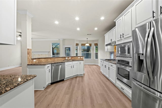 kitchen with white cabinetry, dark stone counters, kitchen peninsula, stainless steel appliances, and backsplash