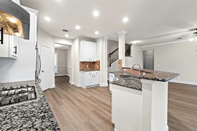 kitchen with range hood, visible vents, dark stone counters, decorative columns, and a sink