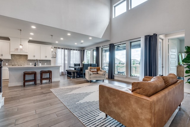 living room featuring high vaulted ceiling, sink, and light wood-type flooring