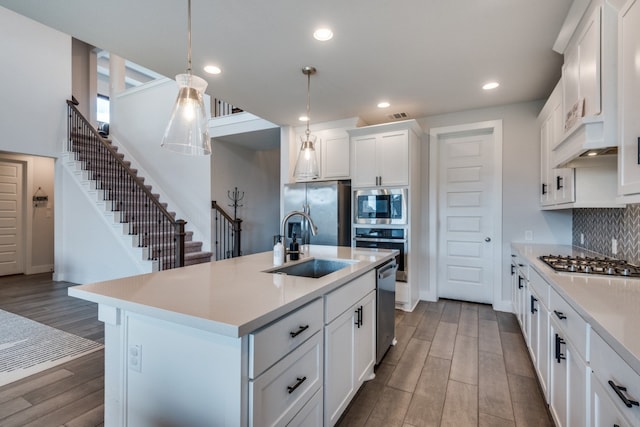 kitchen with pendant lighting, sink, an island with sink, white cabinets, and appliances with stainless steel finishes