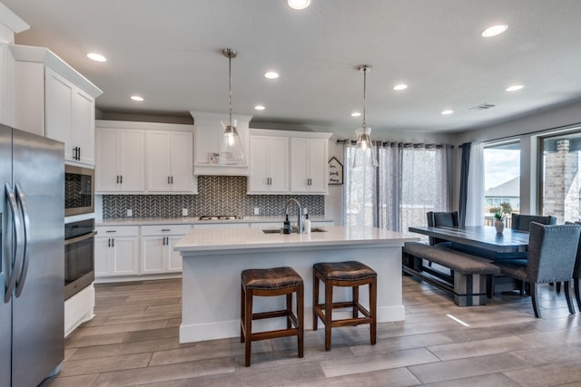 kitchen with a center island with sink, decorative light fixtures, sink, appliances with stainless steel finishes, and white cabinetry