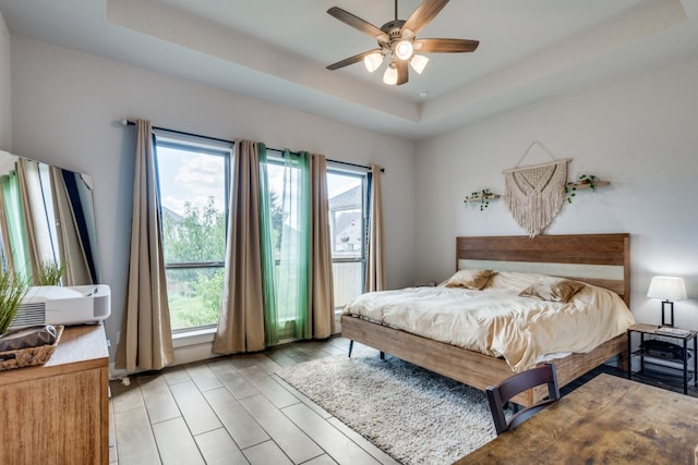 bedroom with a raised ceiling, light hardwood / wood-style floors, and ceiling fan