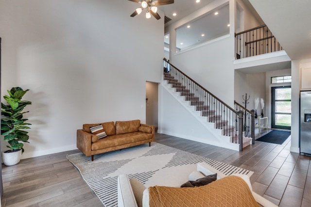 living room with hardwood / wood-style flooring, ceiling fan, and a towering ceiling