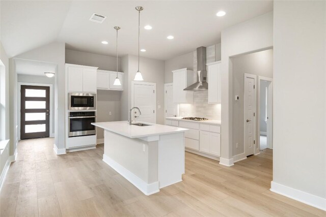 kitchen with backsplash, sink, appliances with stainless steel finishes, light hardwood / wood-style flooring, and wall chimney range hood