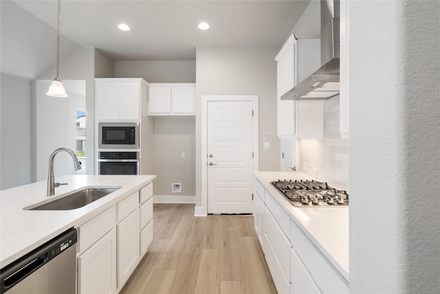 kitchen with light wood-type flooring, wall chimney exhaust hood, white cabinetry, appliances with stainless steel finishes, and sink