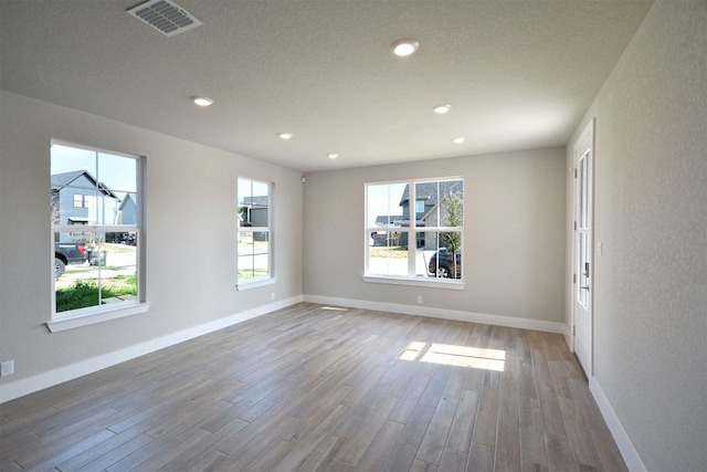 unfurnished room featuring visible vents, a textured ceiling, wood finished floors, recessed lighting, and baseboards