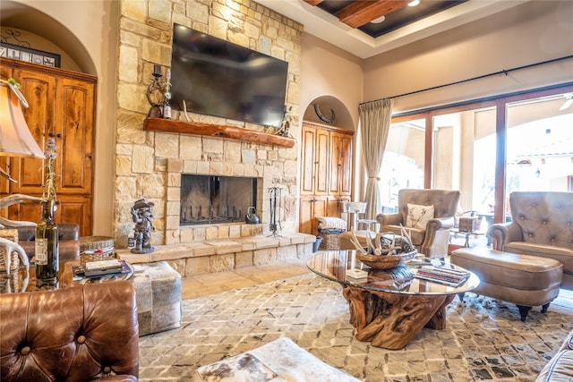 tiled living room with beamed ceiling, a towering ceiling, and a stone fireplace