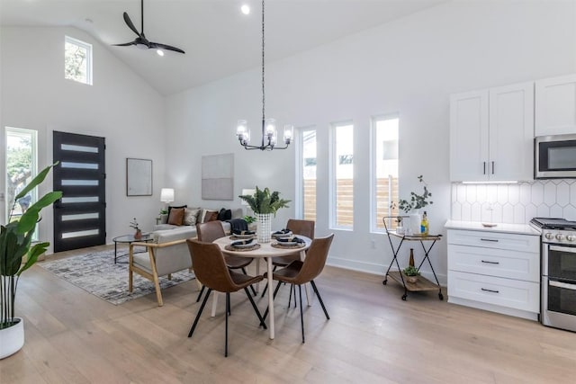 dining area featuring ceiling fan with notable chandelier, high vaulted ceiling, light wood-type flooring, and baseboards