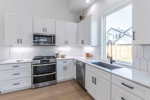 kitchen with light wood-type flooring, backsplash, white cabinets, sink, and stainless steel appliances